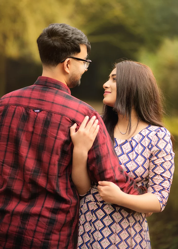 A couple sharing an affectionate gaze during their outdoor photoshoot for women, with the woman holding her partner's arm in a woodland setting.