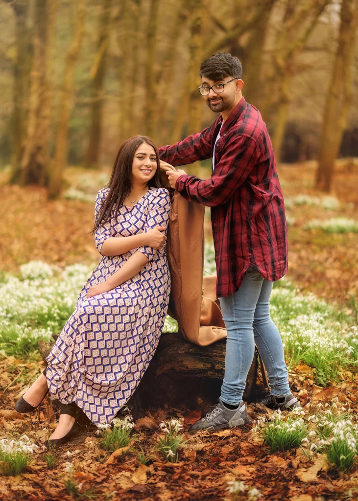 A man placing a coat on a smiling woman’s shoulders during their outdoor photoshoot for women in a woodland setting.