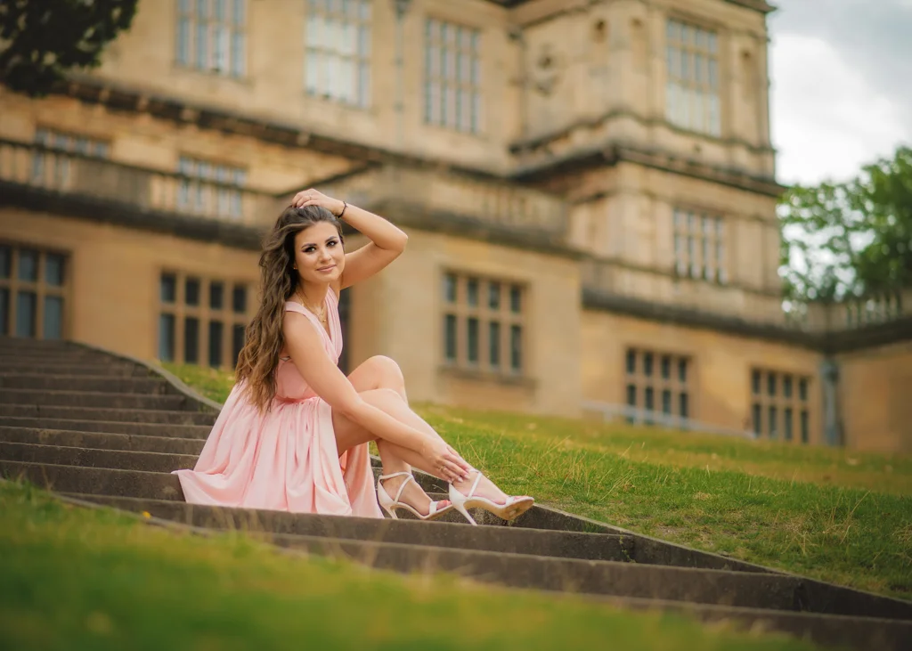 Outdoor female portrait photography with a woman in a pink dress posing on stairs in front of a historic building.