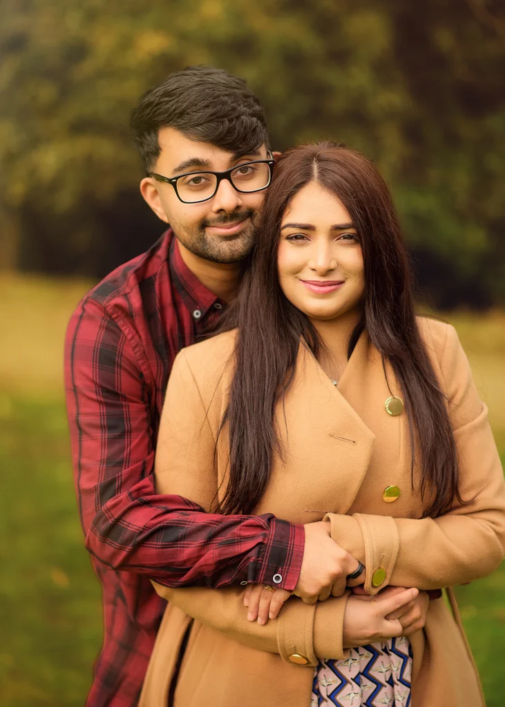 A couple embracing during an outdoor photoshoot, with the woman in a patterned dress and natural surroundings.