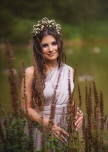 Outdoor female portrait photography featuring a woman in a lavender dress adorned with a floral crown near a lake.