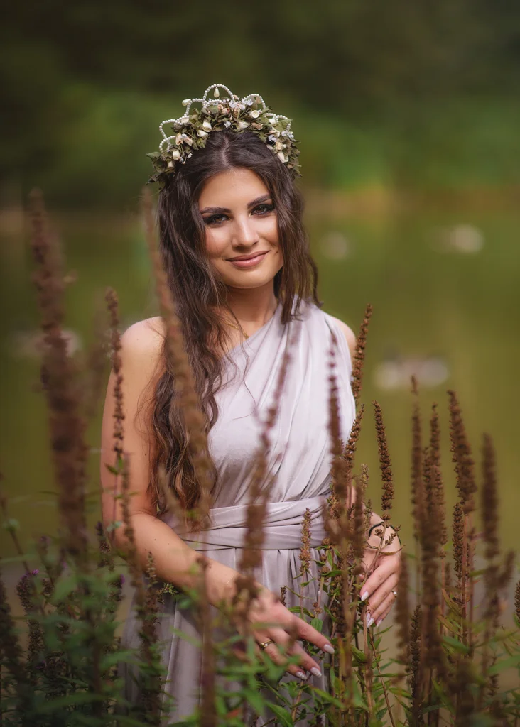 Outdoor female portrait photography featuring a woman in a lavender dress adorned with a floral crown near a lake.