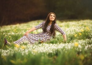 Woman in a patterned dress lying in a field of daffodils and snowdrops during her outdoor photoshoot for women.