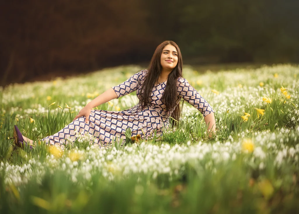 Woman in a patterned dress lying in a field of daffodils and snowdrops during her outdoor photoshoot for women.
