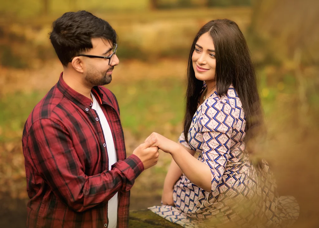 A couple holding hands during a relaxed outdoor photoshoot, with the woman in a patterned dress smiling confidently.