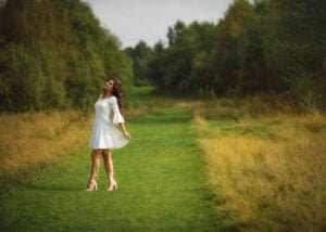Outdoor female portrait photography of a woman in a white dress enjoying a lush green field surrounded by nature.