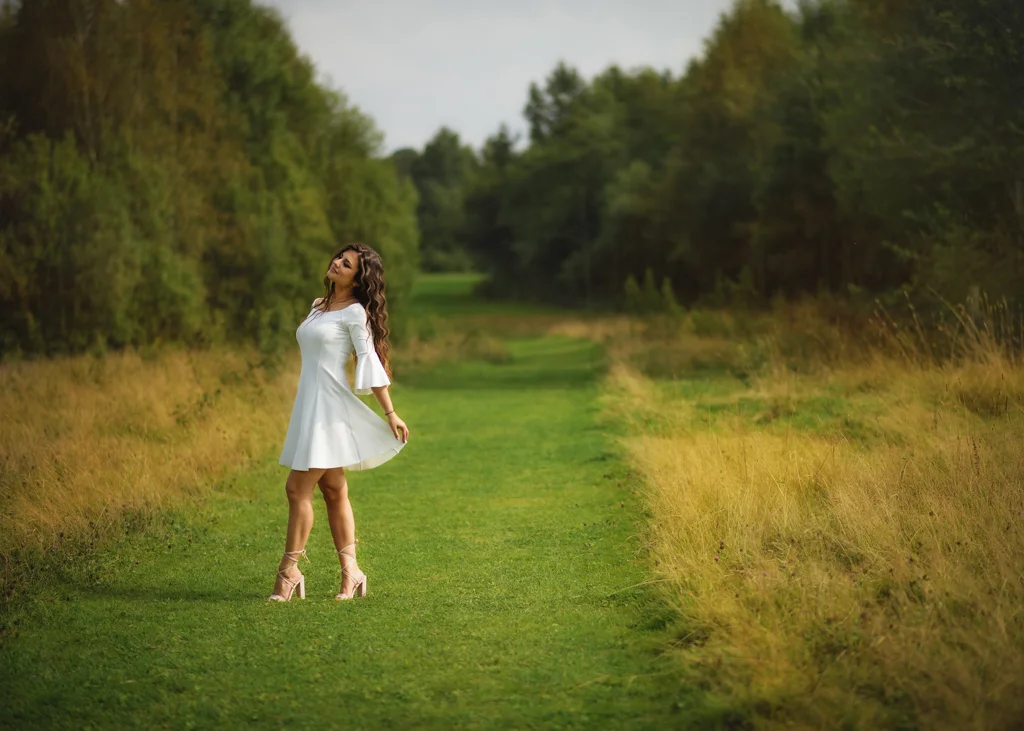 Outdoor female portrait photography of a woman in a white dress enjoying a lush green field surrounded by nature.