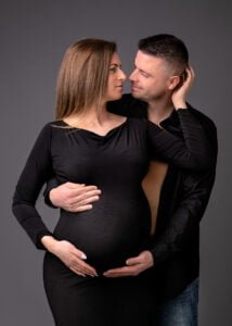 Expectant couple posing during a maternity photoshoot with the mother wearing a black dress in Nottingham.