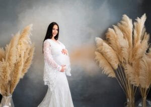 Expectant mother in a white lace dress posing for a maternity photoshoot with pampas grass in Nottingham.