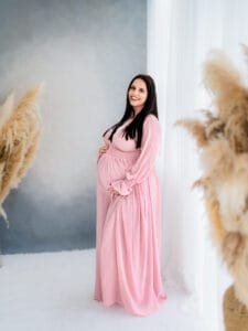 Maternity photoshoot featuring an expectant mother in a pink dress, standing next to pampas grass in Nottingham studio.