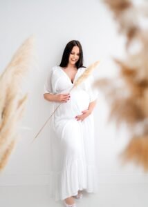 Maternity photoshoot featuring an expectant mother in a flowing white dress holding pampas grass in Nottingham.
