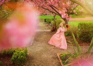 Professional portrait of a woman in a pink dress under spring blossoms.
