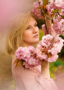 Close-up of a mature woman in a pink dress, her gaze soft and thoughtful as she gently touches cherry blossoms, symbolizing the delicate beauty of spring in Nottingham.