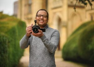 Photographer holding a camera in a manicured garden for a business photography shoot.