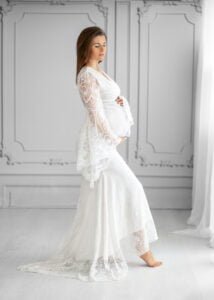 Expectant mother in a white lace maternity dress posing during a studio maternity photoshoot in Nottingham.