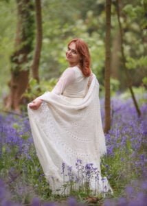Graceful red-haired mature woman in a flowing white dress enjoying a bluebell forest in Nottingham.