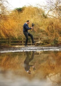 Photographer capturing business photography with natural reflections by a wooded stream.