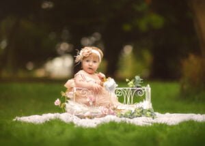 Toddler sitting on a blanket in a whimsical outdoor setting during her 1st Birthday Photoshoot.