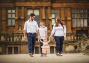 Family walking hand-in-hand with their toddler during an outdoor 1st Birthday Photoshoot at Wollaton Hall.