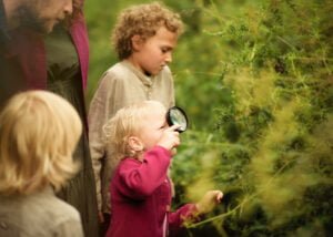 Young girl exploring nature with a magnifying glass during an outdoor family photoshoot in Nottingham.