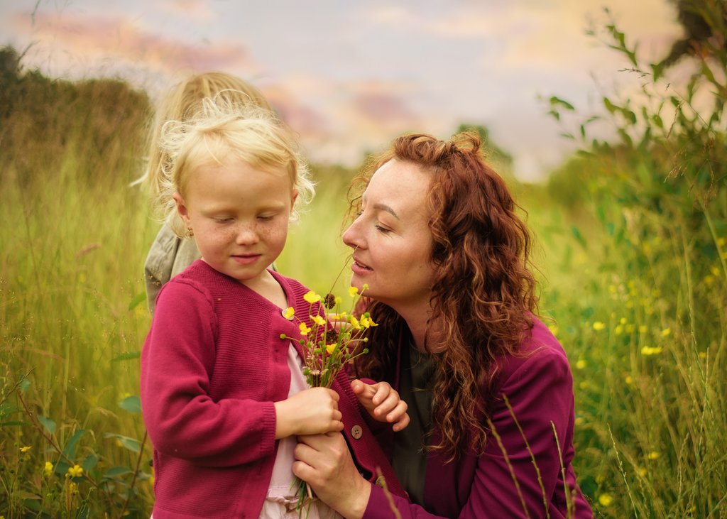 A tender moment in Nottingham's countryside captured during a family photography session as a mother lovingly looks at her child holding wildflowers.