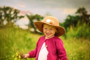 Smiling girl wearing a hat and holding flowers during an outdoor family photoshoot in Nottingham.