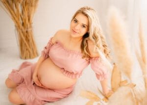 Close-up maternity portrait of a mom-to-be in a pink dress during a baby bump photoshoot, surrounded by pampas grass.