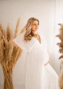 Solo maternity portrait with a flowing white dress and pampas grass during a baby bump photoshoot in Nottingham studio.