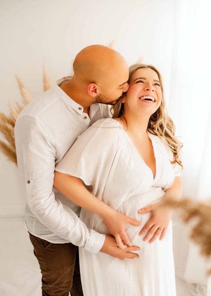 Joyful maternity photo featuring a couple laughing during their baby bump photoshoot in a Nottingham studio.Joyful maternity photo featuring a couple laughing during their baby bump photoshoot in a Nottingham studio.