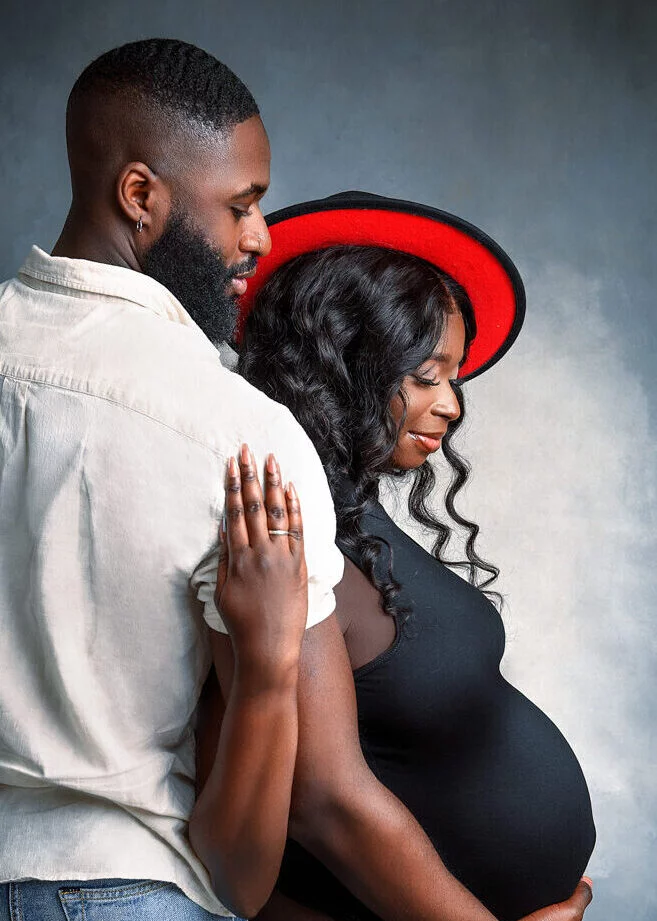 Romantic baby bump photoshoot featuring a couple with a bold red hat, celebrating maternity moments in Nottingham studio.