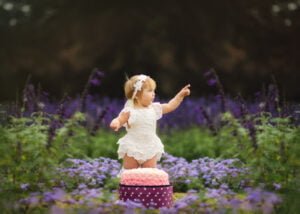 Toddler standing in a garden with a cake smash backdrop during her 1st Birthday Photoshoot.