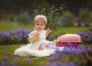 Toddler enjoying a pink cake smash during her 1st Birthday Photoshoot in a flower-filled garden at Wollaton Hall Park.