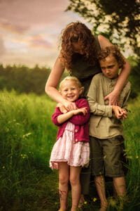 Mother hugging two children in a meadow during an outdoor family photoshoot in Nottingham.