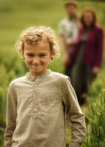Young boy smiling in the foreground with his parents in the background during an outdoor family photoshoot in Nottingham.