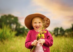 Smiling girl holding wildflowers while wearing a hat during an outdoor family photoshoot in Nottingham.