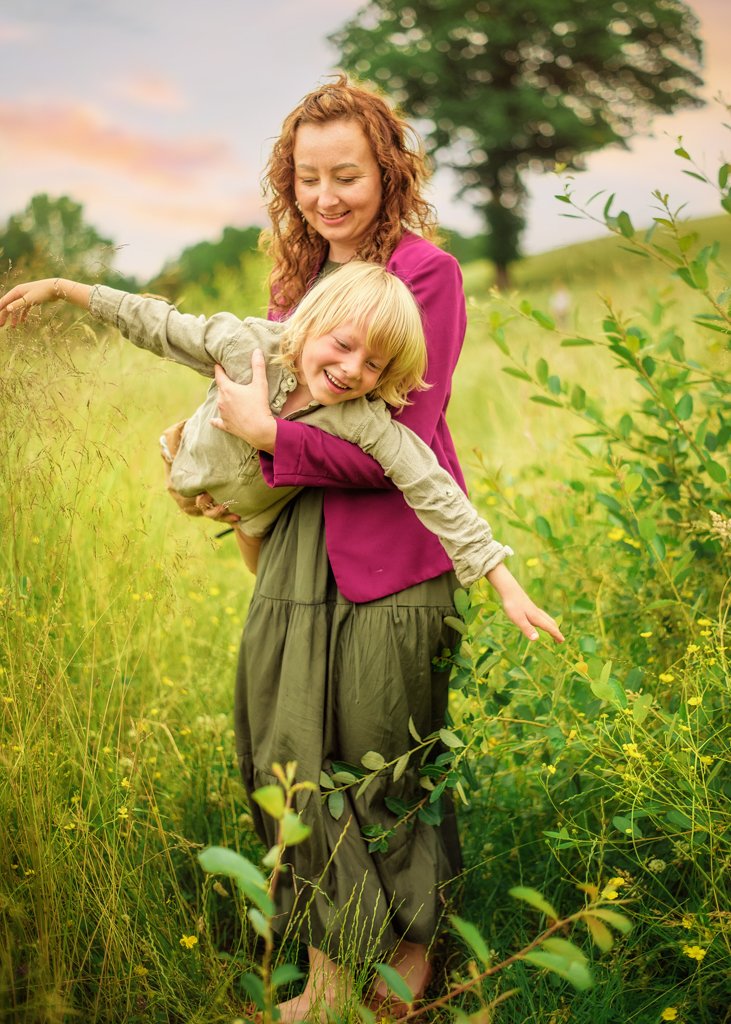 Mother's tender embrace around her child in a Nottingham meadow, under a sunlit sky, captures the essence of family photography.