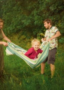 Smiling child swinging in a hammock during a family photoshoot in Nottingham countryside.