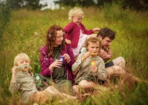 Family blowing bubbles together in a sunny meadow during an outdoor family photoshoot in Nottingham.