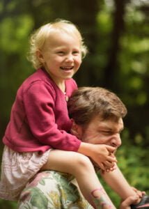 Daughter riding on her father’s shoulders, laughing during an outdoor family photoshoot in Nottingham.