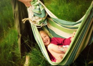Child laughing in a hammock during an outdoor family photoshoot in Nottingham countryside.