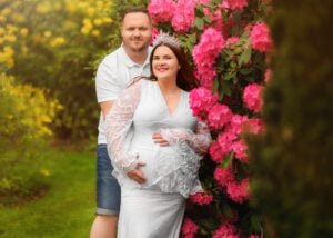 Expecting couple embracing near vibrant pink flowers during a maternity and family photoshoot in Nottingham.