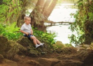 A young child sitting on a rock near a forest stream during an outdoor family photoshoot in Nottingham.
