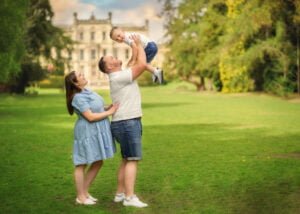 Parents lifting their child in the air, smiling joyfully, during an outdoor family photoshoot at a historic Nottingham location.