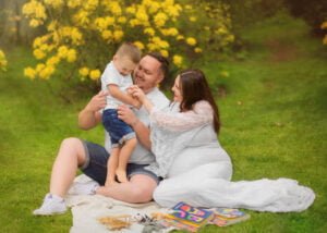 Parents playing with their young child on a picnic blanket during a family photoshoot in Nottingham’s colorful garden.