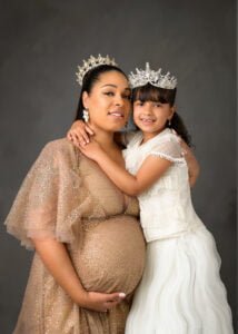 Expectant mother in a gold lace dress surrounded by pampas grass during a maternity photography session.