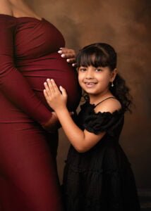 Young daughter touching her pregnant mother’s belly during a maternity photography session.