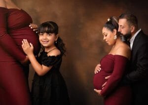 Family with daughter embracing pregnant mother captured by a professional maternity photographer.