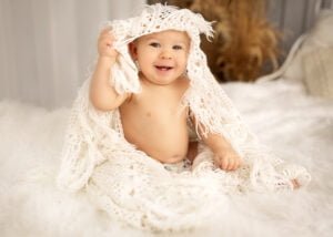 Smiling baby playing with a crocheted blanket during a professional baby photography session.