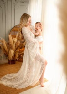 Mother cradling her baby near a window with boho-style decor in a baby photography session.