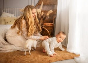Baby crawling while mother and dog look on in a baby photography session with natural light.